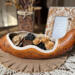 A rustic table centerpiece featuring a real gourd carved into a long decorative bowl filled with wood flowers. It sits on a burlap cloth.